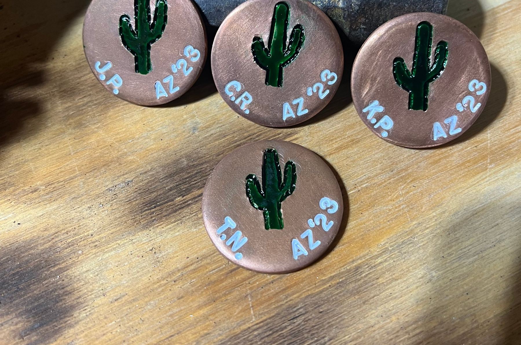 Copper ball markers with dot-punched cactus designs leaning on a stamping hammer